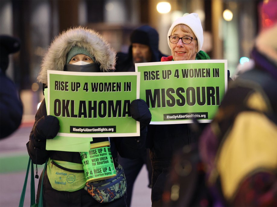 Two women wearing winter clothing hold up green signs that reads "Rise up 4 women in Missouri"